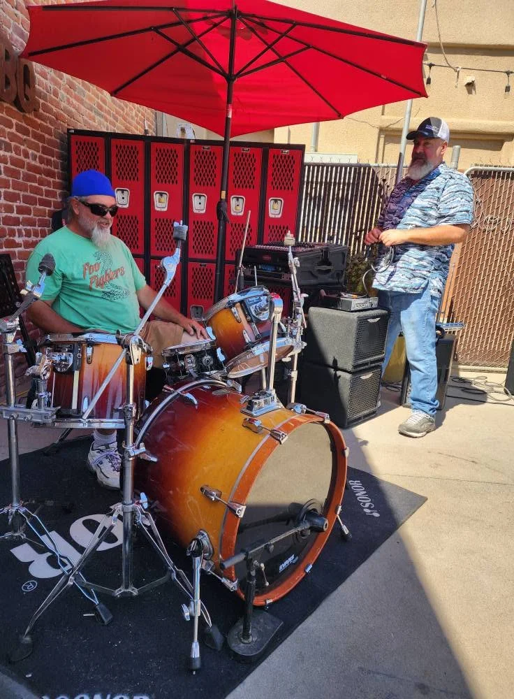 Live music performance with drummer and guitarist under a red umbrella