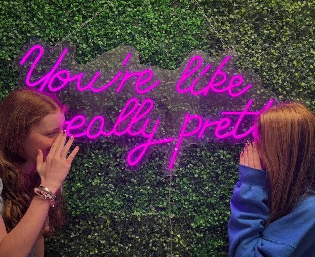 Two friends laughing in front of a neon sign