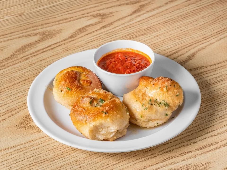 Three golden brown stuffed bread balls served with a side of marinara sauce in a small white bowl.