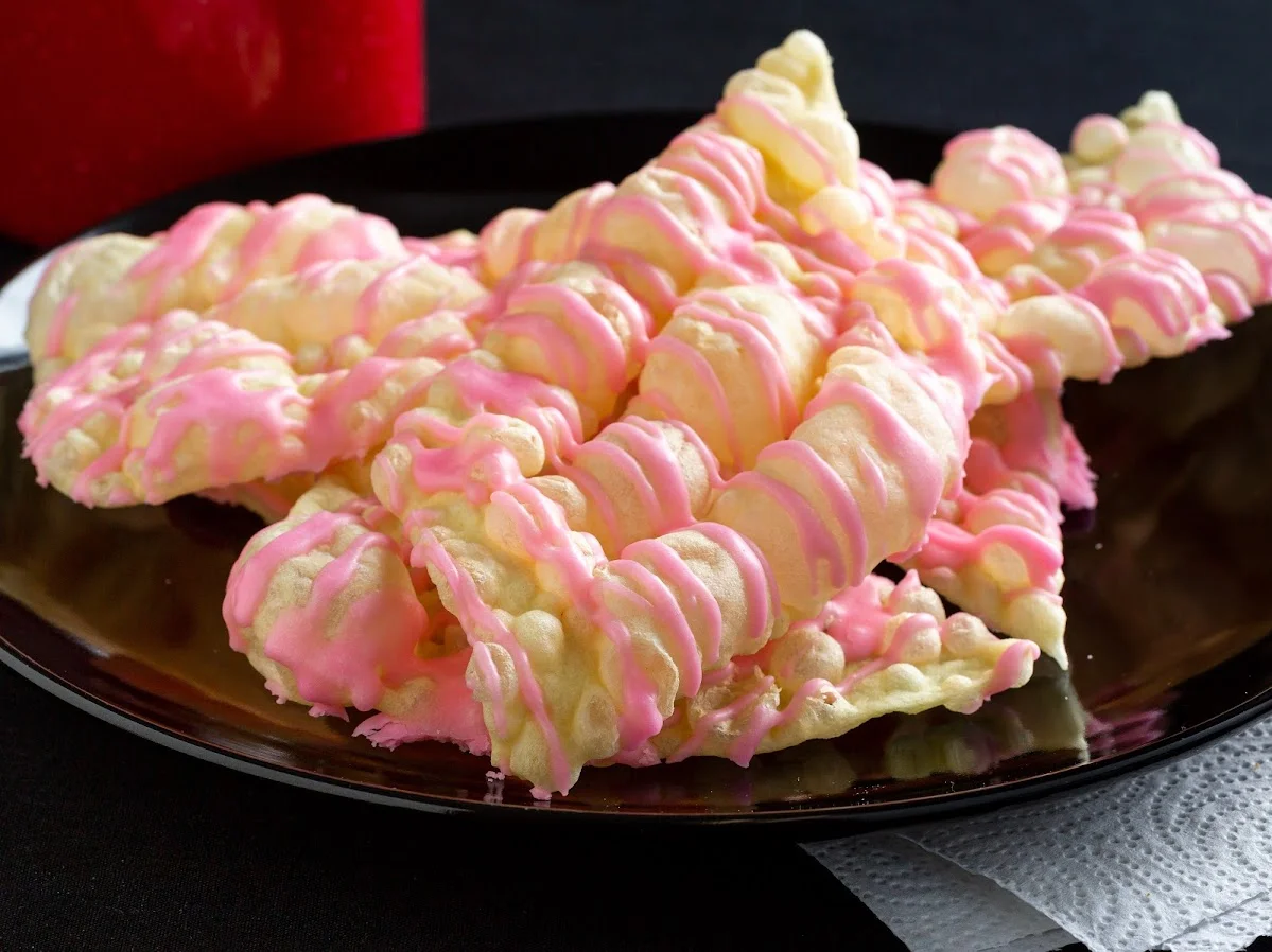 Colorful pink and white Italian carnival cookies on a black plate