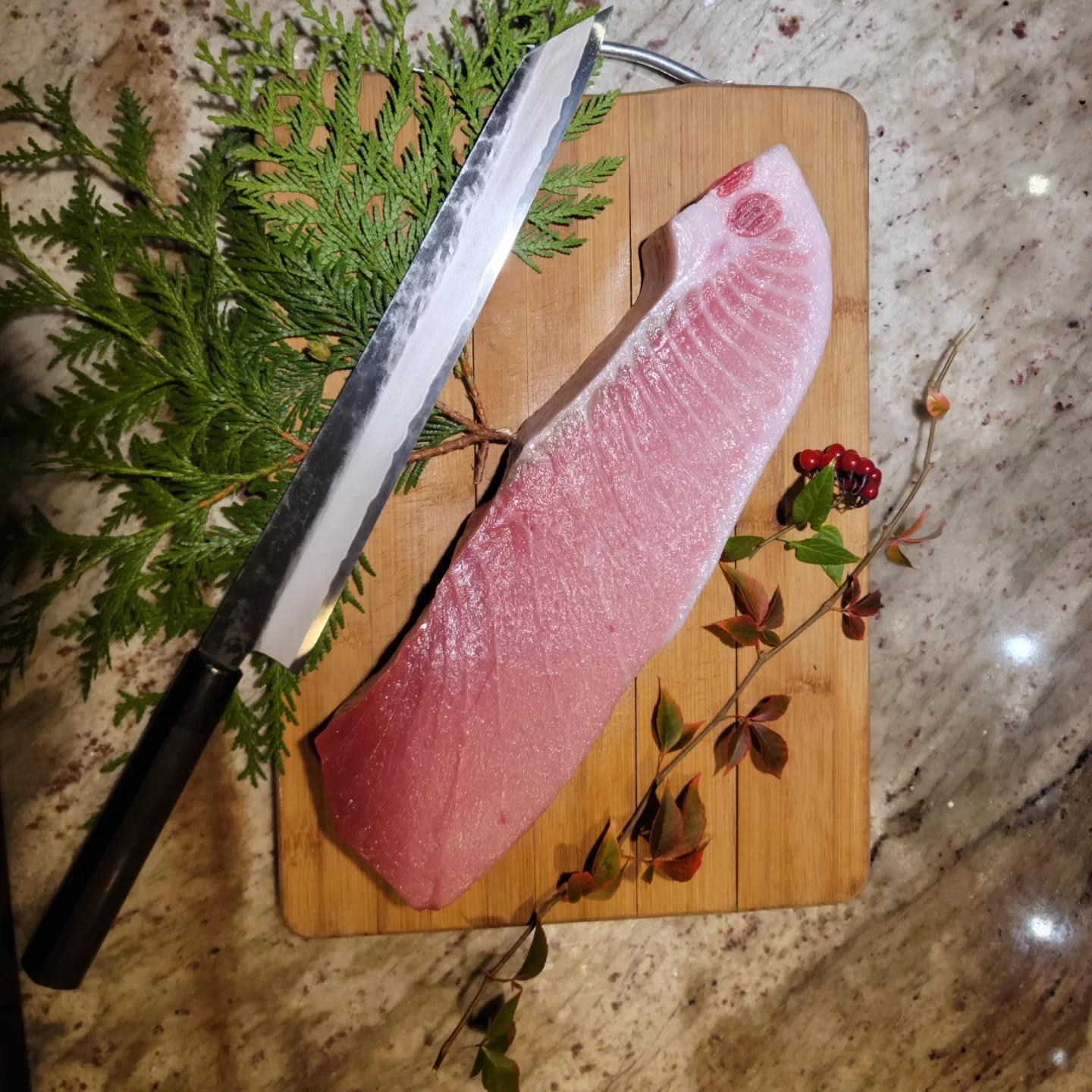 A fresh piece of tuna displayed on a wooden cutting board alongside a sharp knife and foliage accents.