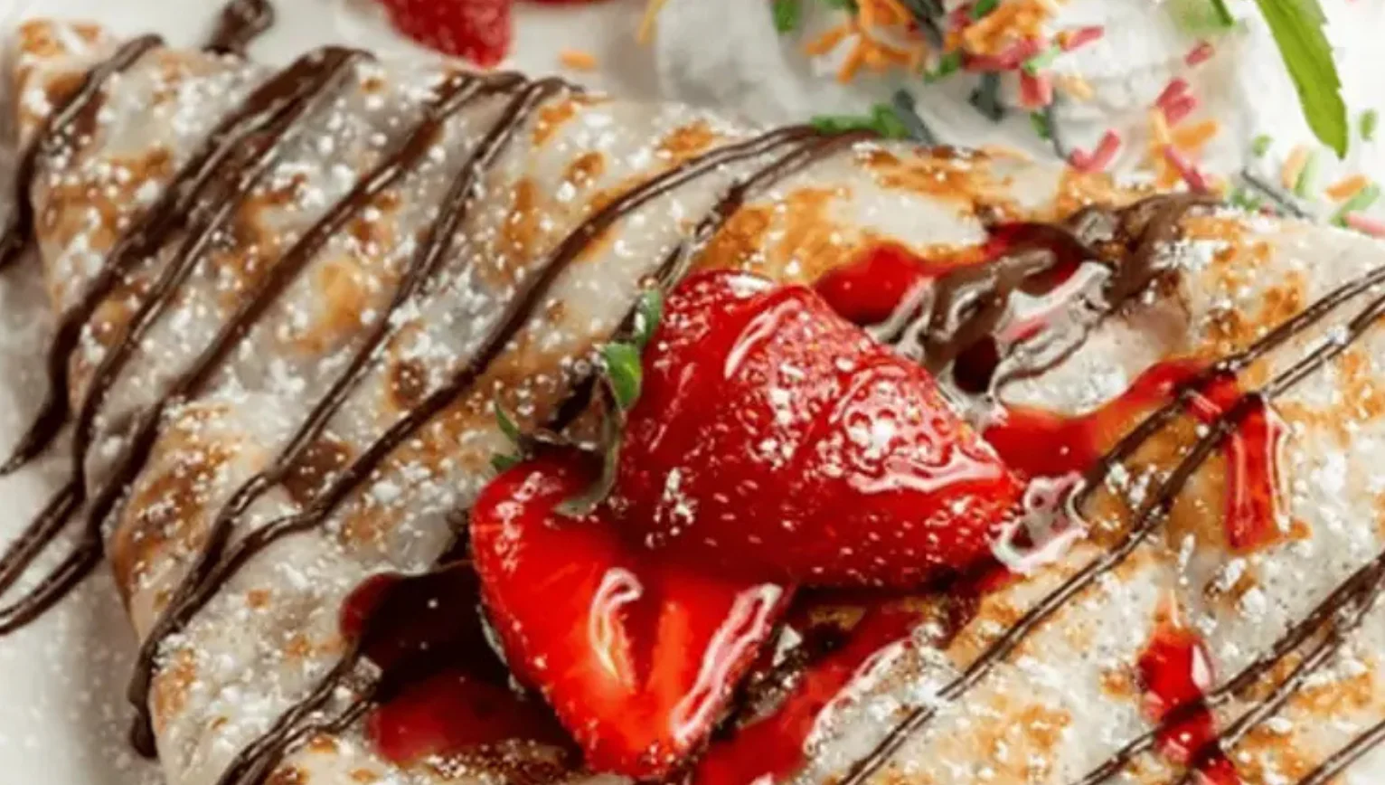 Delicious strawberry dessert crepe drizzled with chocolate sauce