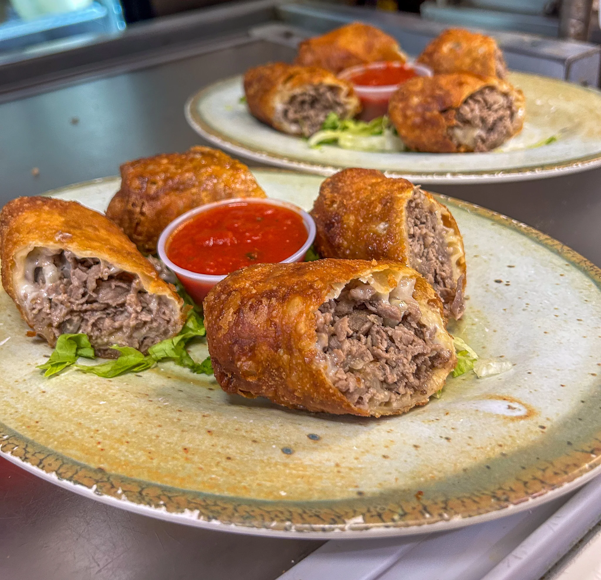 Crispy golden egg rolls cut open to reveal chopped cheesesteak filling, served with marinara sauce