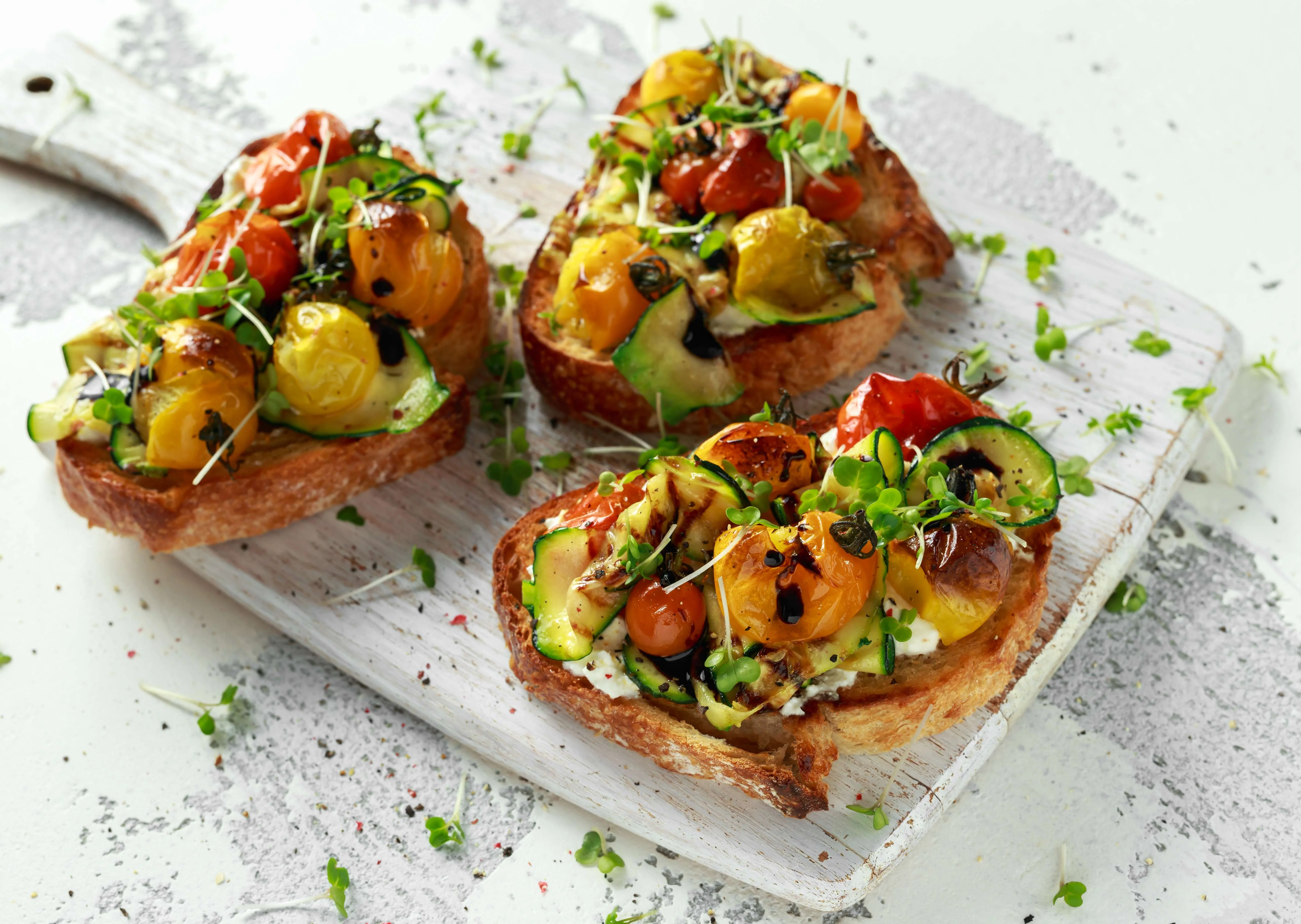 Three slices of toasted bread topped with colorful roasted vegetables.