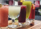 A selection of colorful cocktails displayed on a wooden tray, each garnished with fruit, showcasing a variety of flavors.