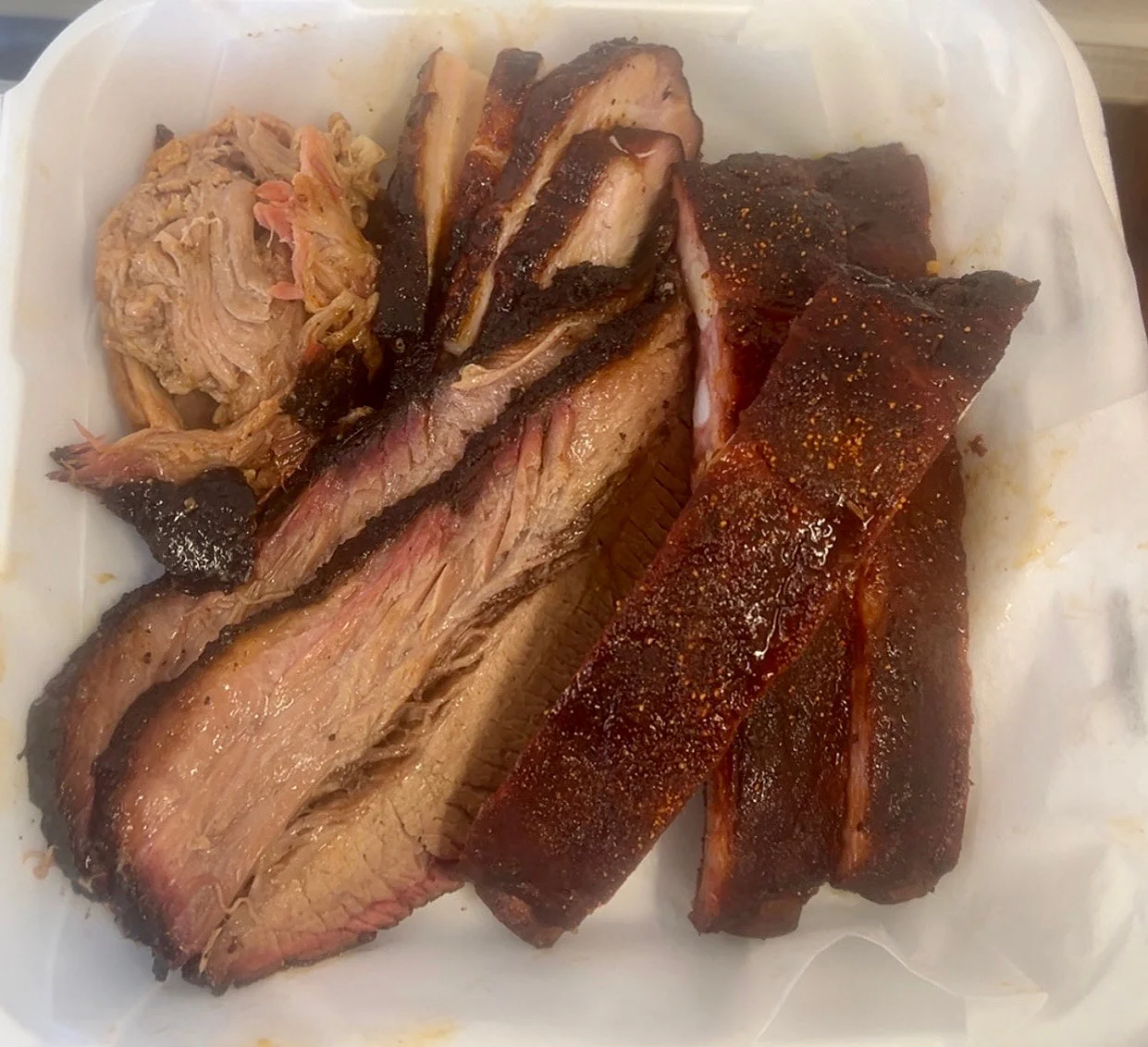 A tantalizing assortment of BBQ meats including brisket, pulled pork, and ribs, presented in a takeout container.