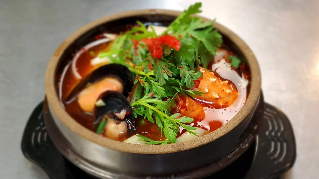 Korean seafood tofu soup with shrimp, mushrooms, and fresh herbs in traditional stone bowl at Sushi Kim 2 restaurant