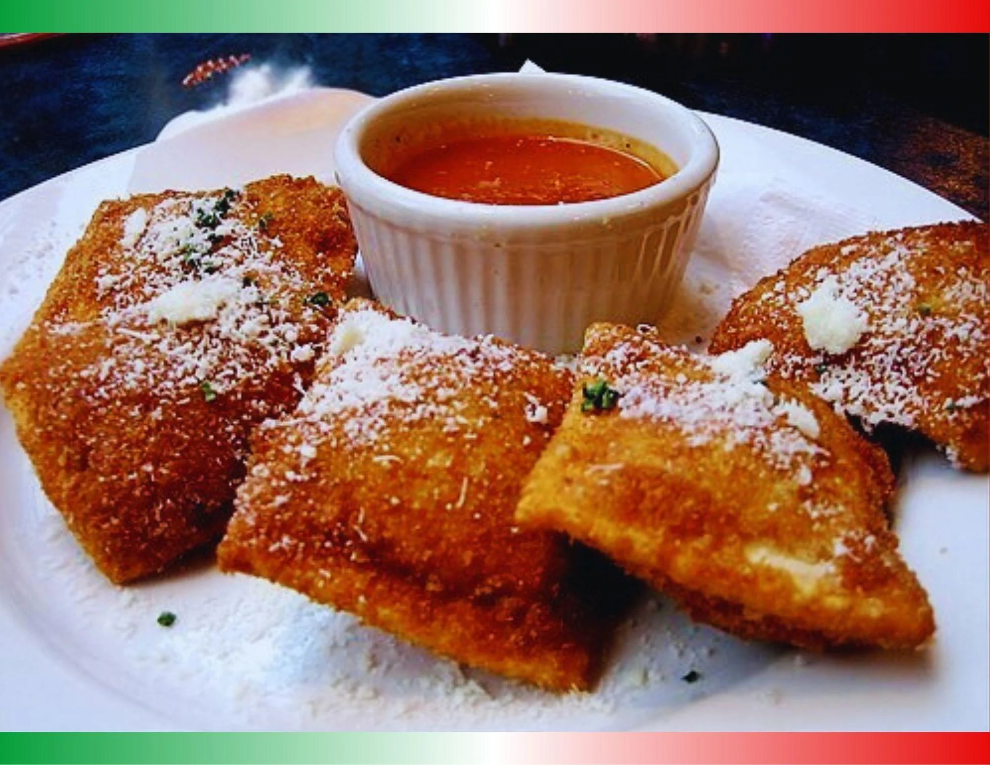 A plate of fried ravioli sprinkled with cheese, served with a small bowl of marinara sauce.
