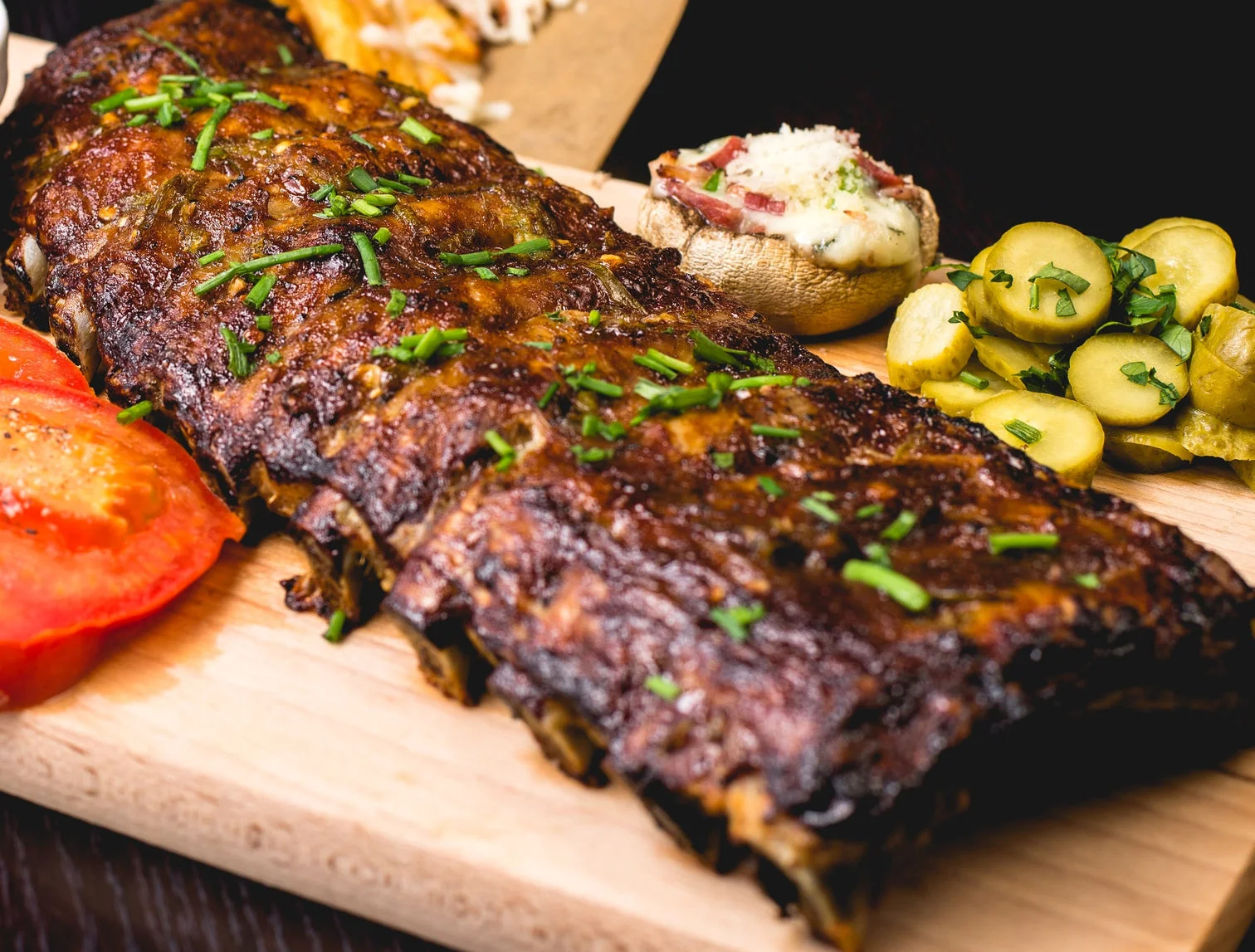 Delicious grilled ribs with pickles and tomato on a wooden platter.
