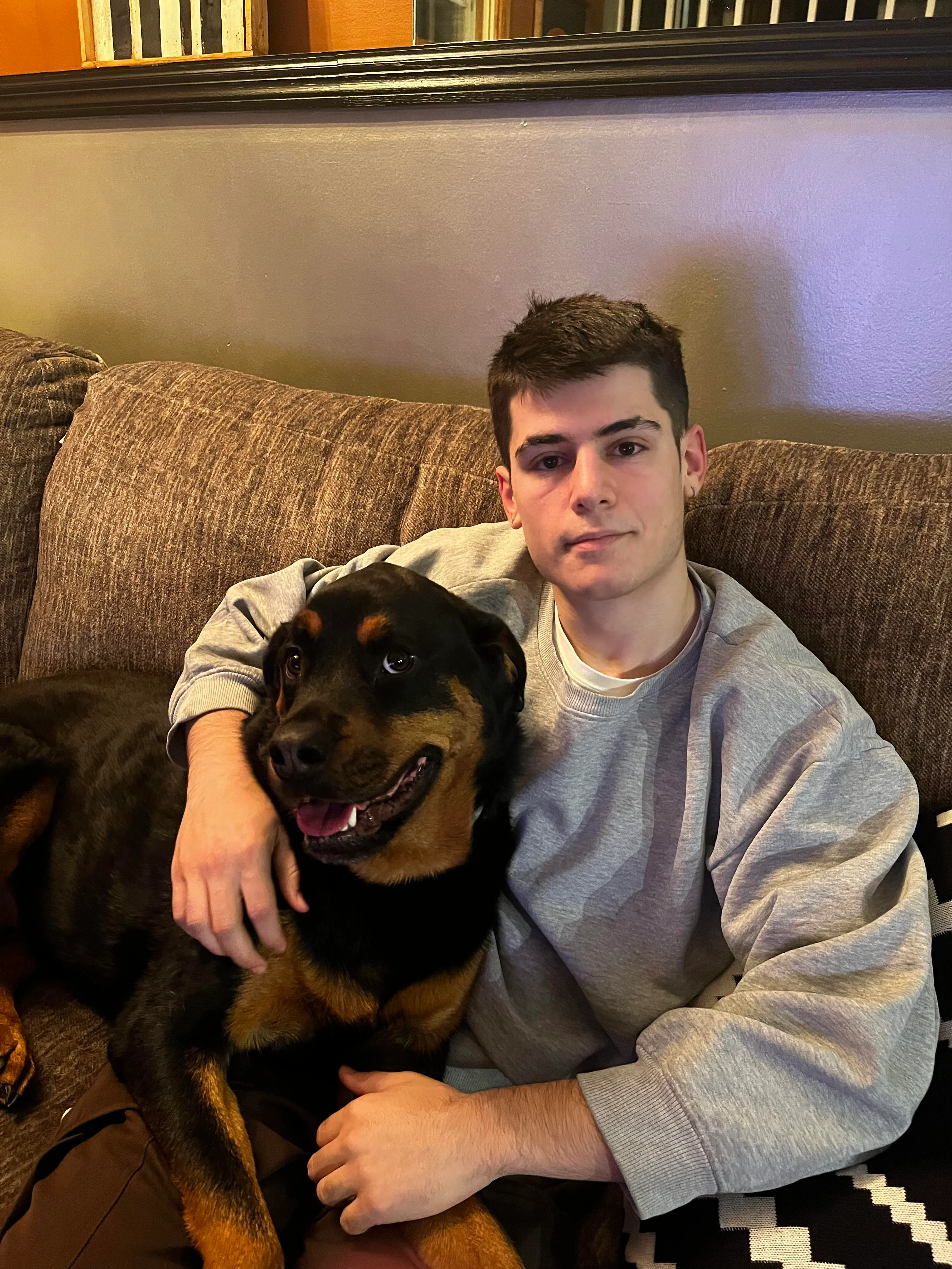 Young man relaxing on a couch with a Rottweiler dog