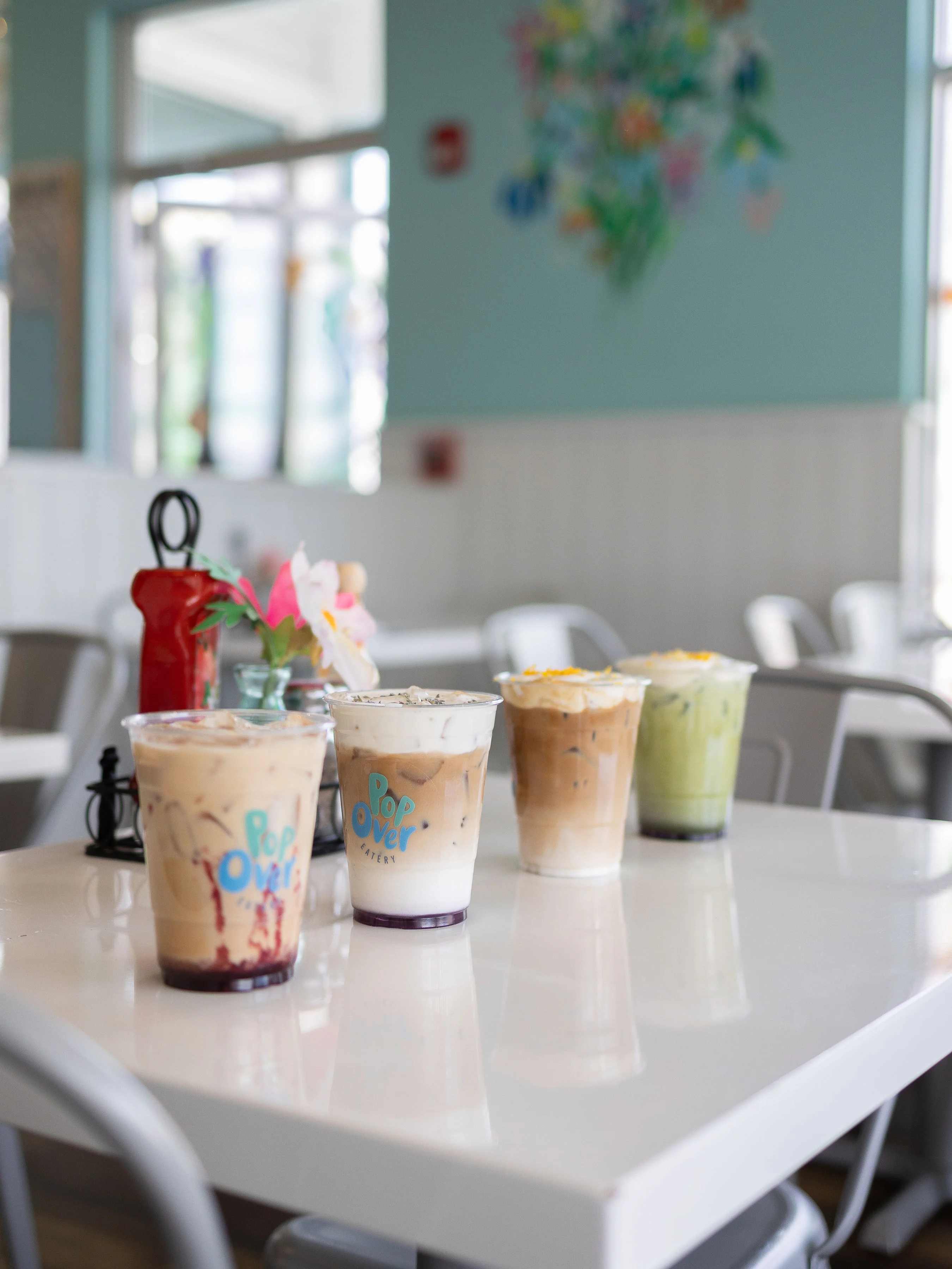 Multiple clear cups filled with different varieties of iced coffee, each with unique toppings, displayed on a table.