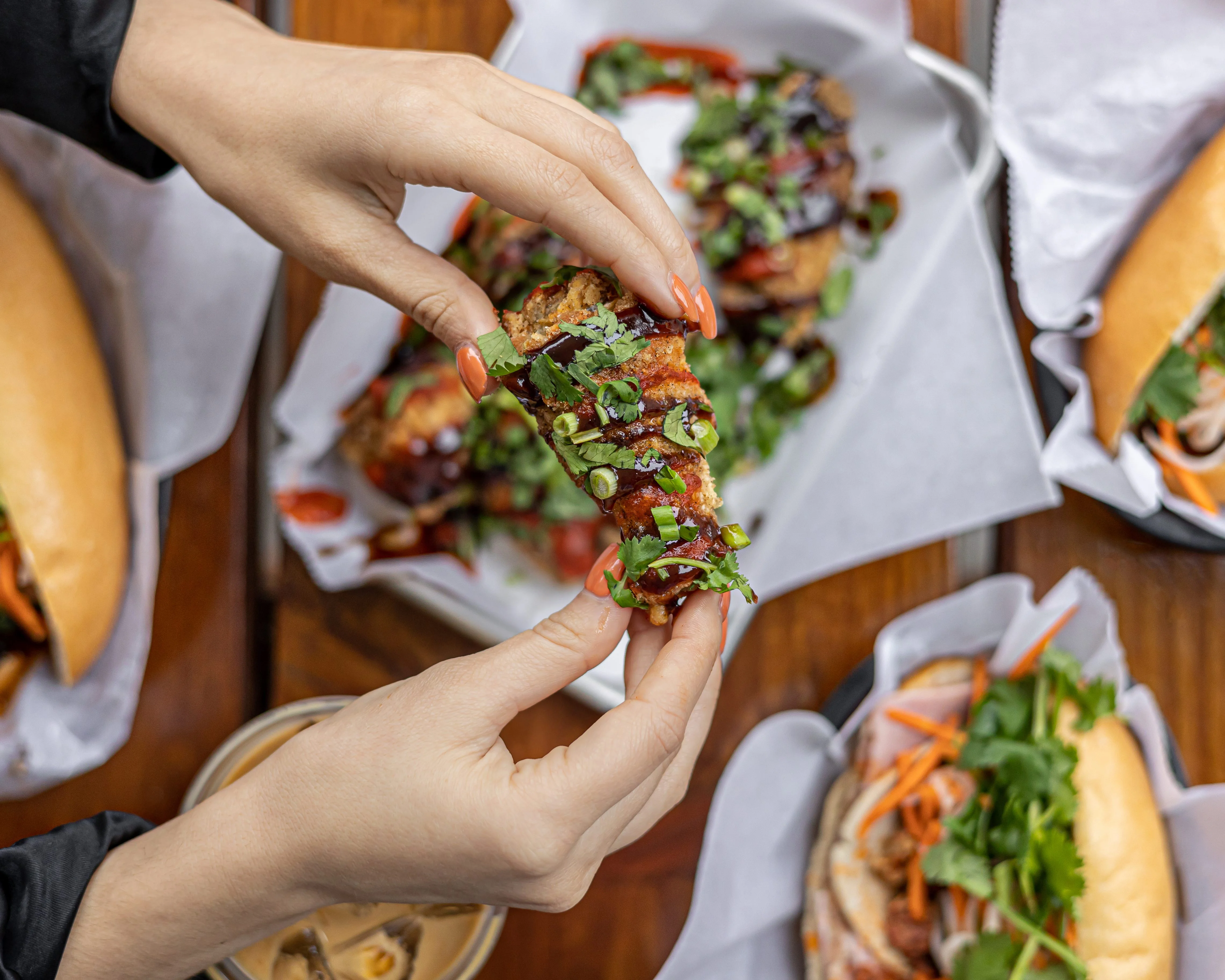 A hand holding a flavorful dish topped with herbs and sauces.