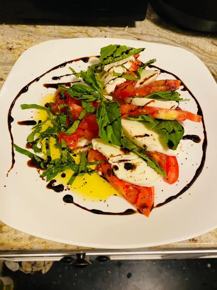 A colorful Caprese salad featuring layers of fresh mozzarella, tomatoes, and basil, drizzled with balsamic glaze and arranged beautifully on a white plate.