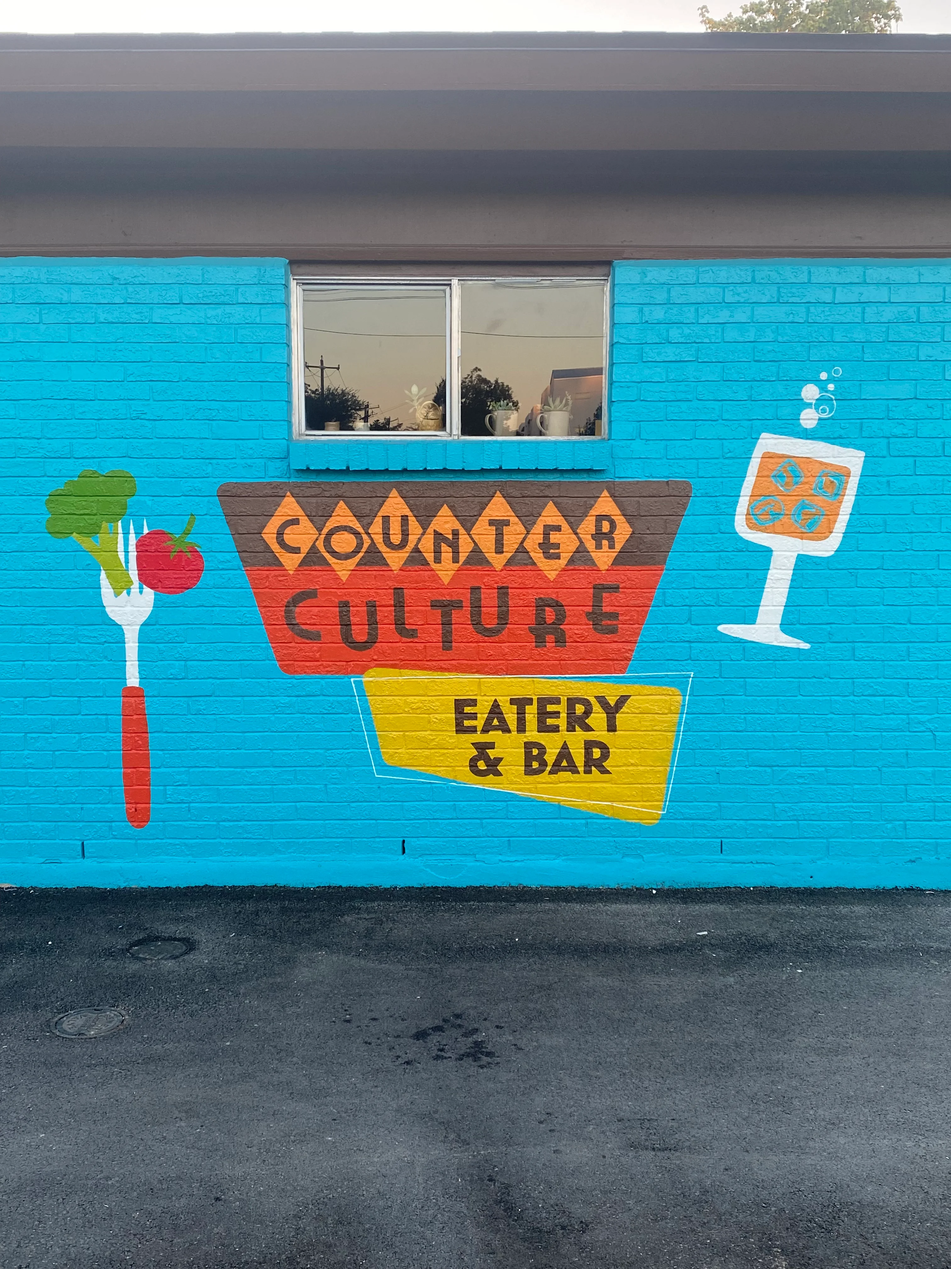 A colorful mural on the exterior of a building featuring a fork, a tomato, drinks, and the words 'Counter Culture Eatery & Bar'.