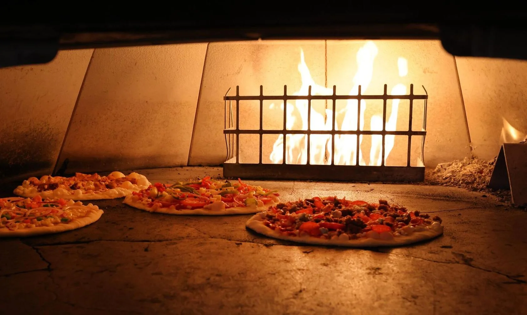 Wood-fired oven with stacked firewood and pizza being prepared.
