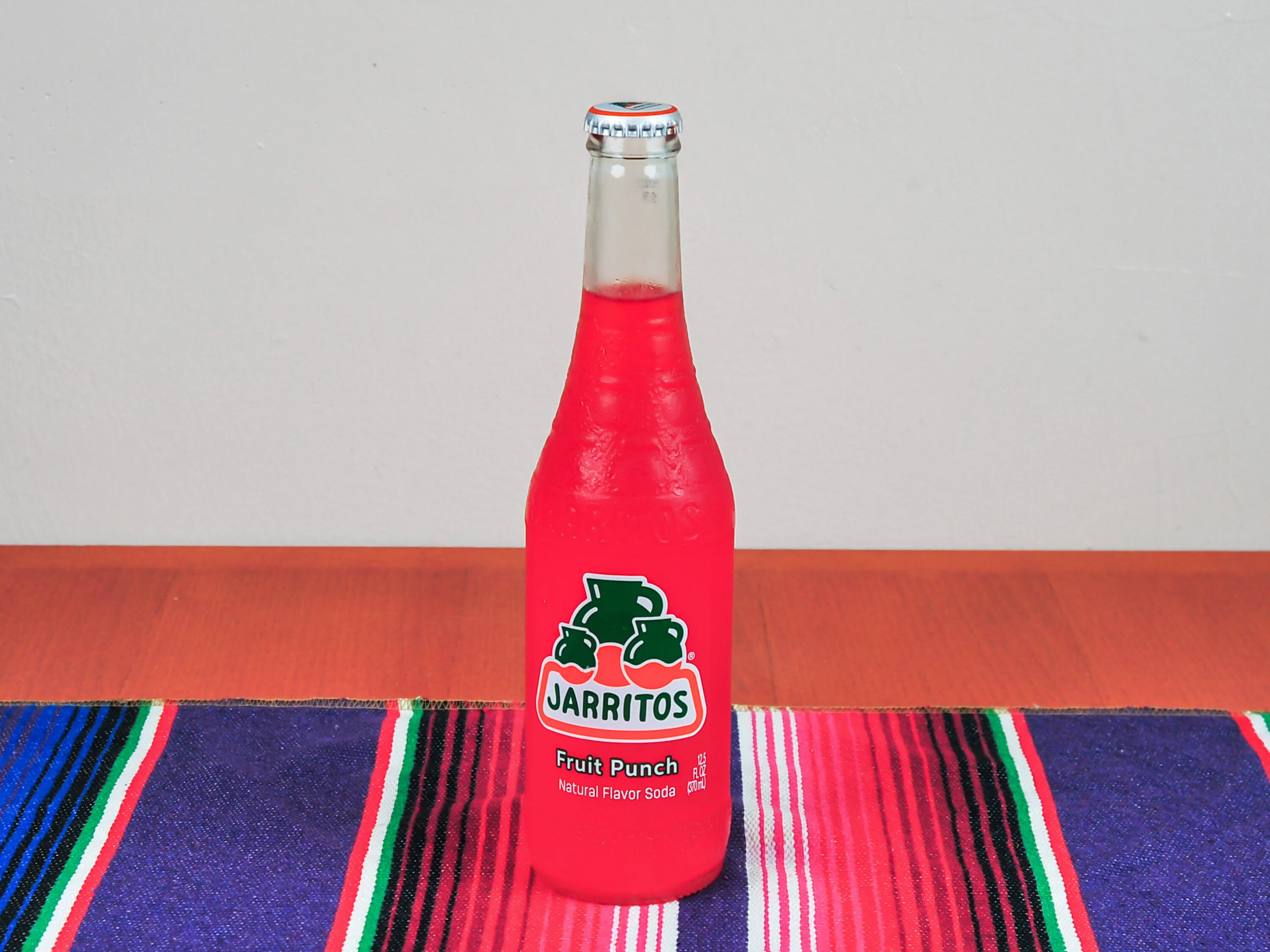 A colorful bottle of fruit punch soda with a vibrant red hue, sitting on a striped textile.