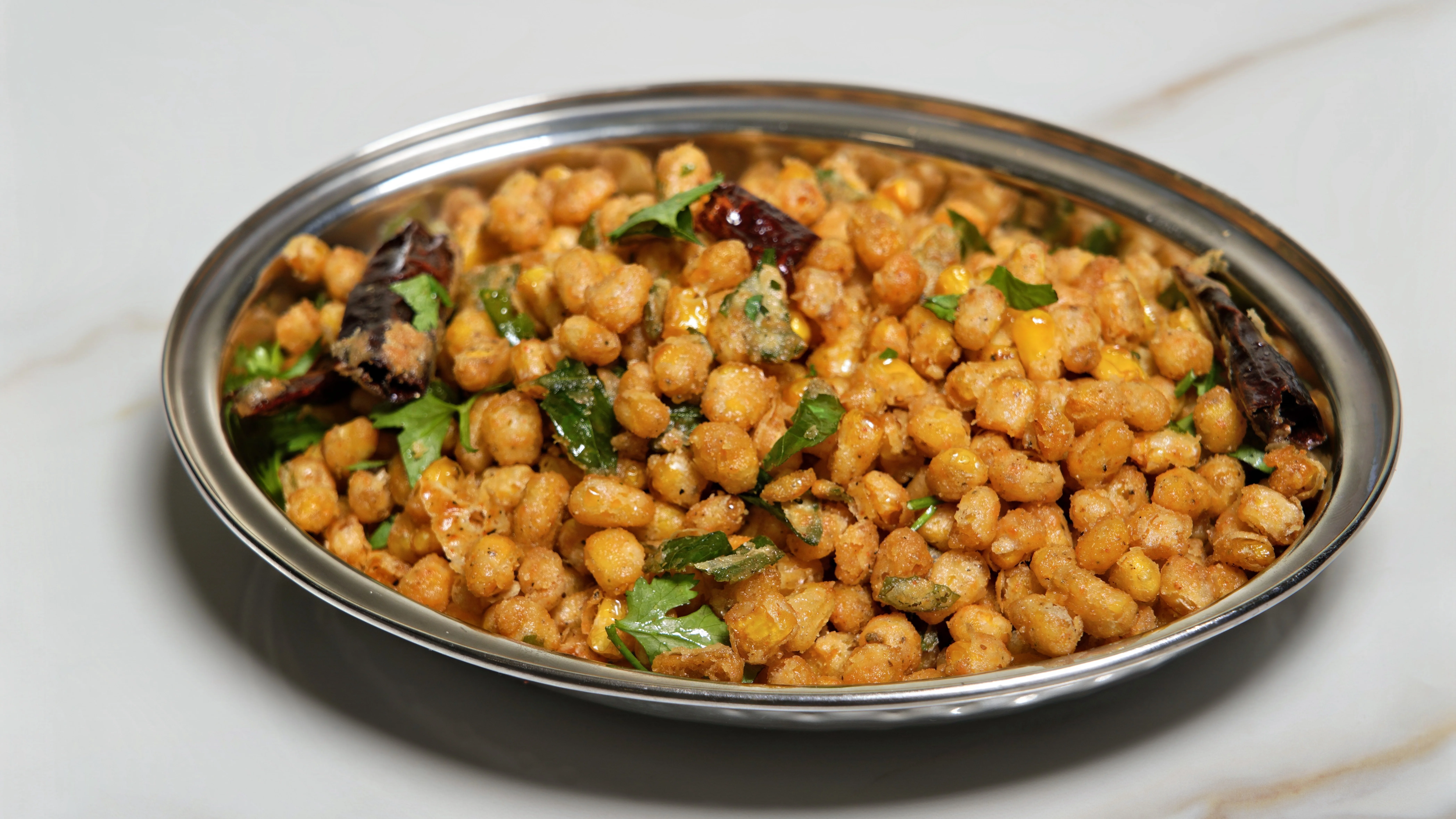 A silver bowl filled with spiced chickpeas garnished with fresh coriander and dried red chilies, showcasing a vibrant mix of textures and colors.