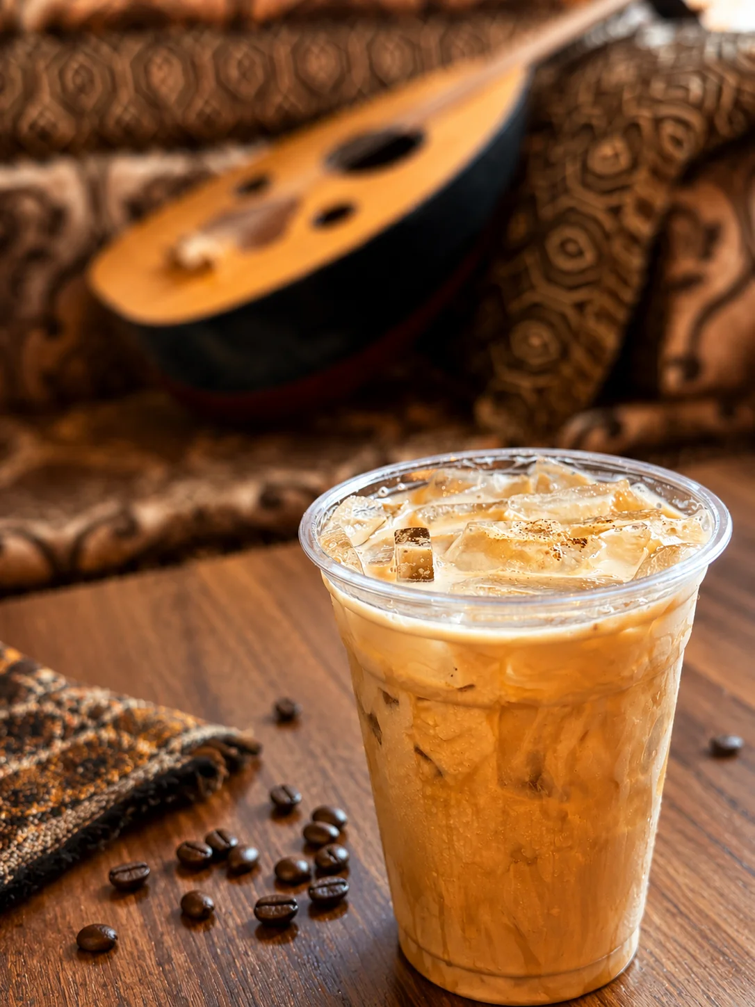 Iced coffee in a clear cup with coffee beans and an instrument in the background.