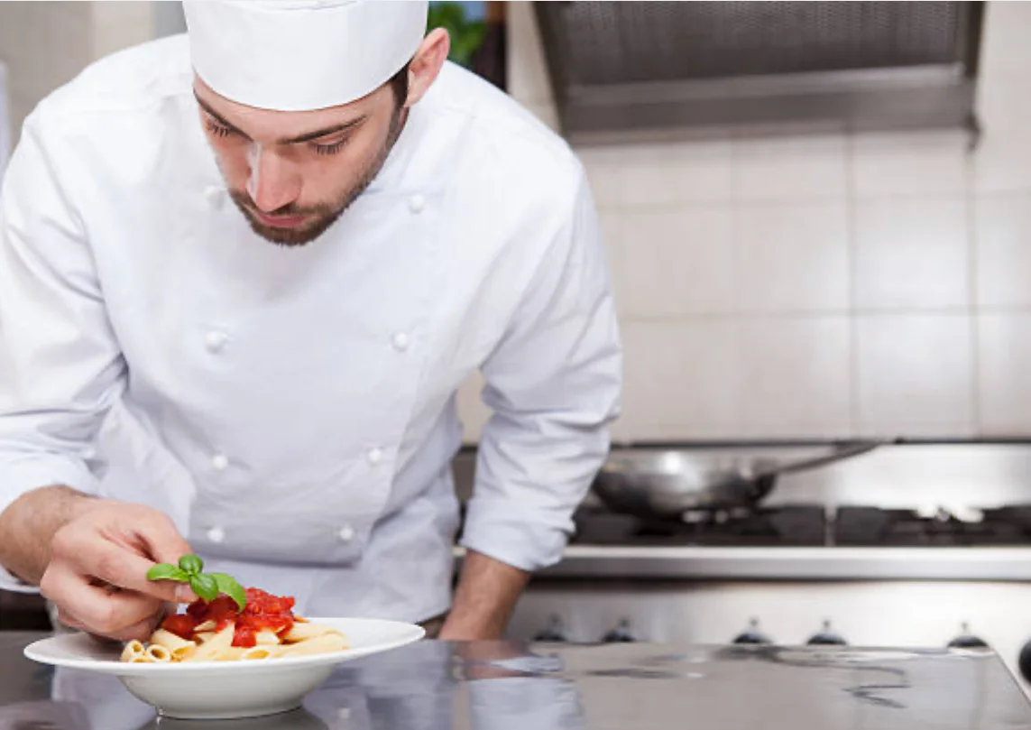 Chef plating Italian pasta with tomato sauce and basil