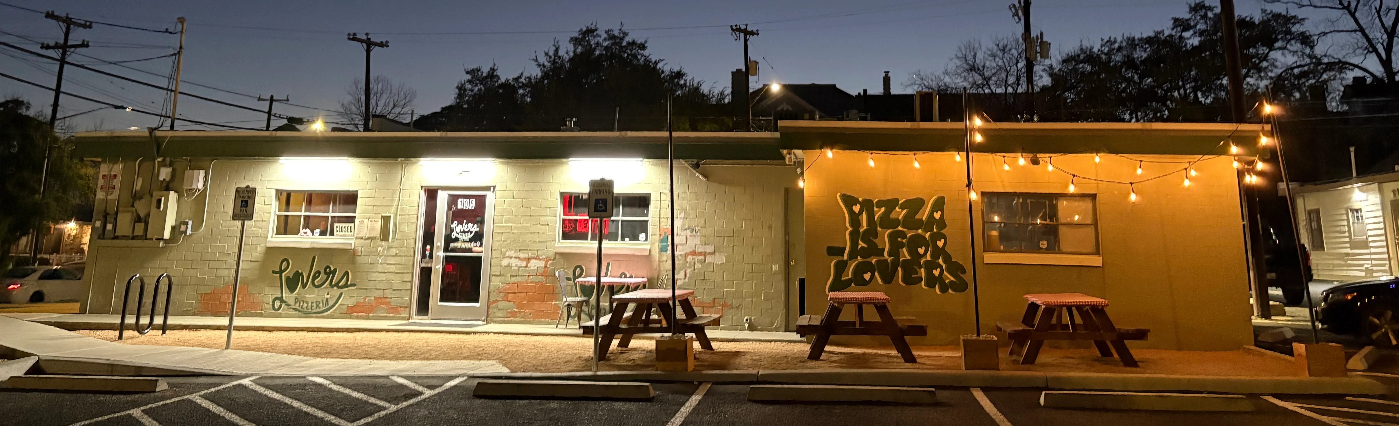 Exterior of a pizzeria at dusk with string lights and a crescent moon.