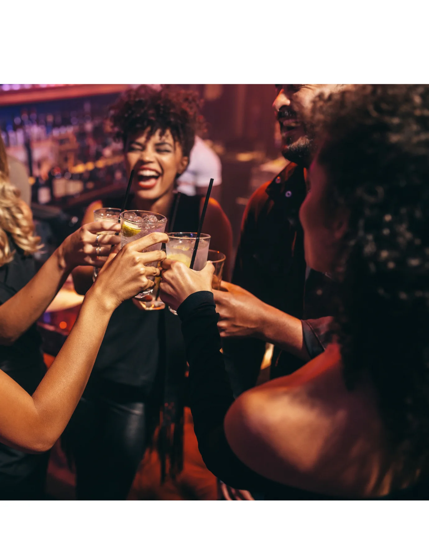 Group of friends toasting with cocktails at a lively bar