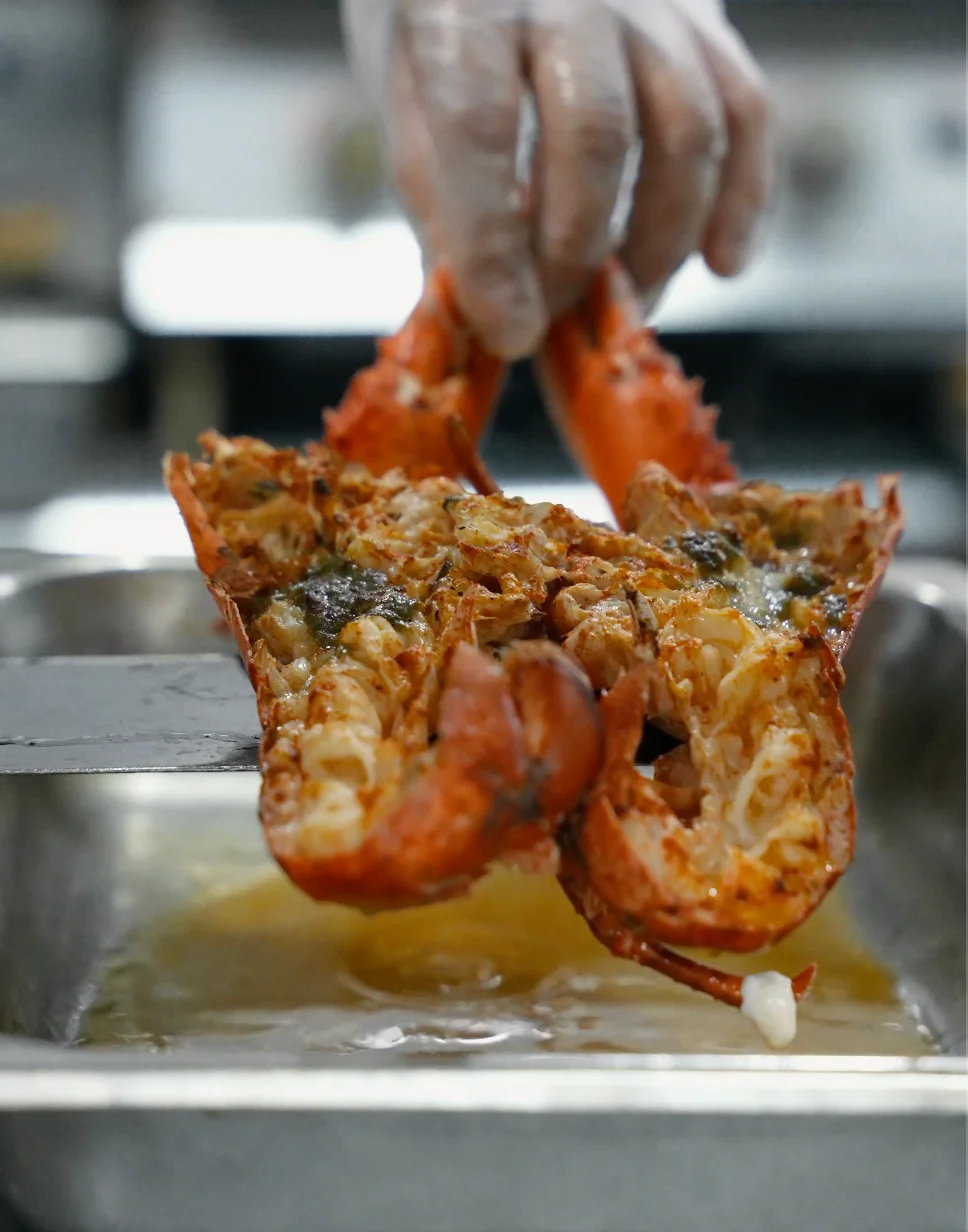 A chef holding a cooked lobster above a tray in a kitchen setting.