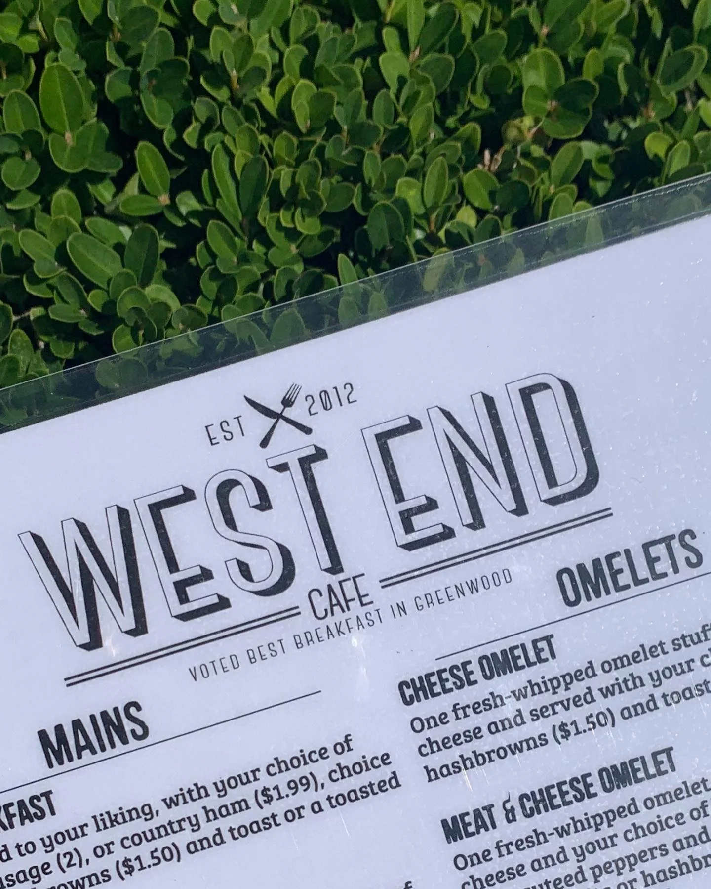 A menu from West End Cafe featuring various breakfast options including omelets and sides, displayed against a green background.
