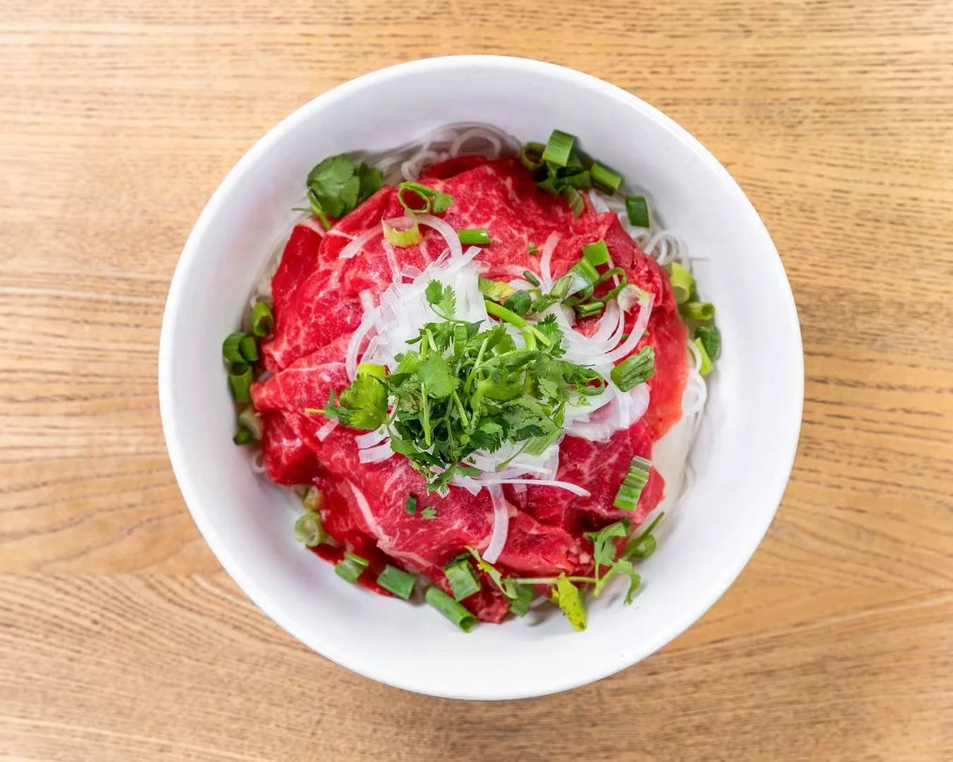 Bowl of fresh beef with herbs and noodles on a wooden table