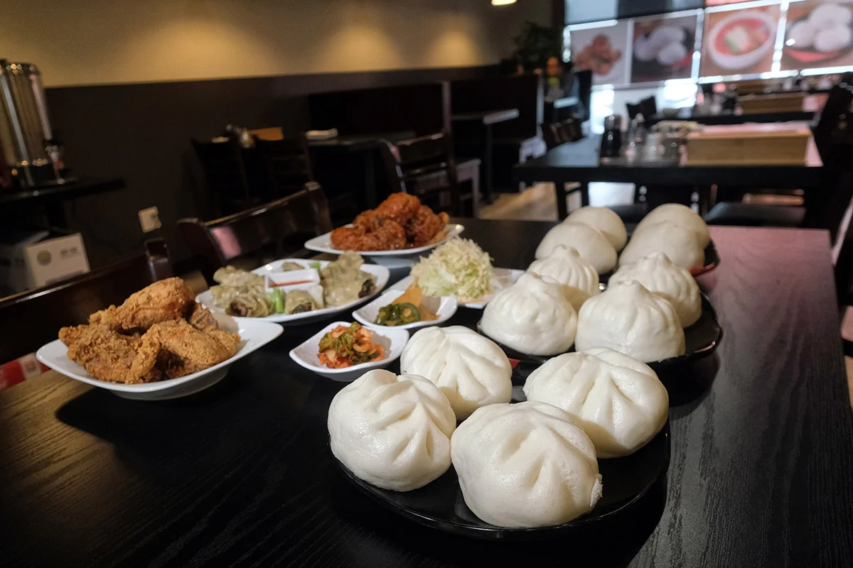 A table with various Asian dishes including bao buns, fried chicken, and dumplings.