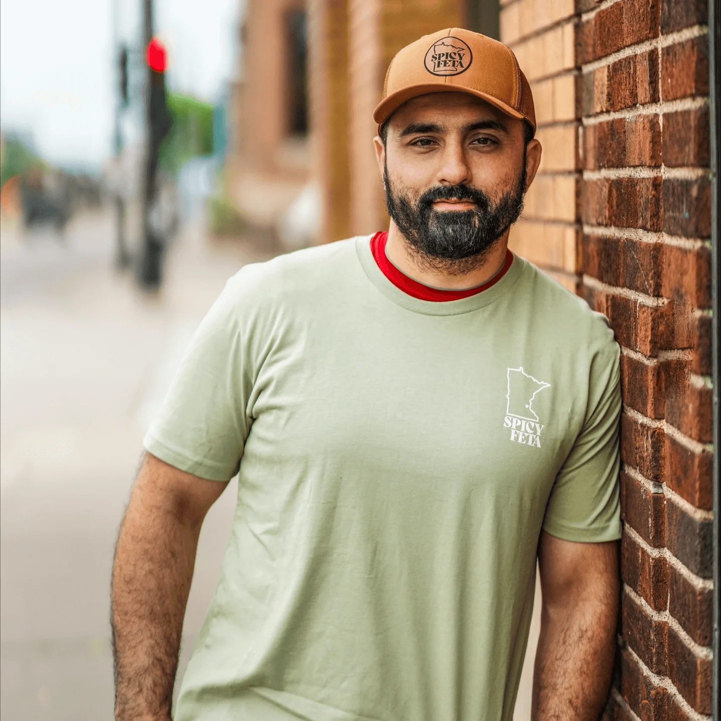 Man in Spicy Feta shirt posing against a brick wall