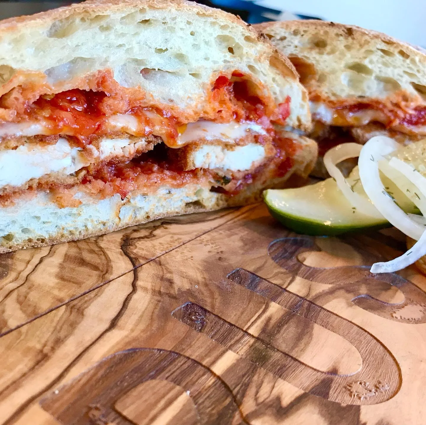 A close-up of a sandwich filled with sauce and chicken, accompanied by onion and lime on the side.