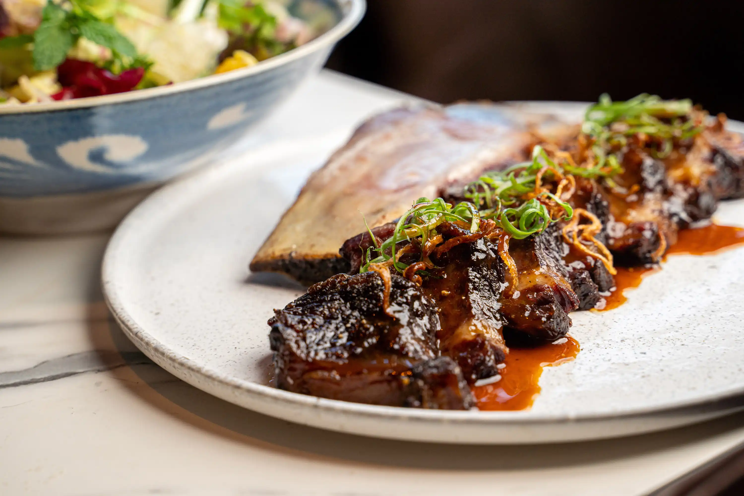 WAGYU SMOKED BEEF RIB Beef-Palm Sugar Glaze, Chicory Salad, Pink Lady Apple, Onion, Herbs.