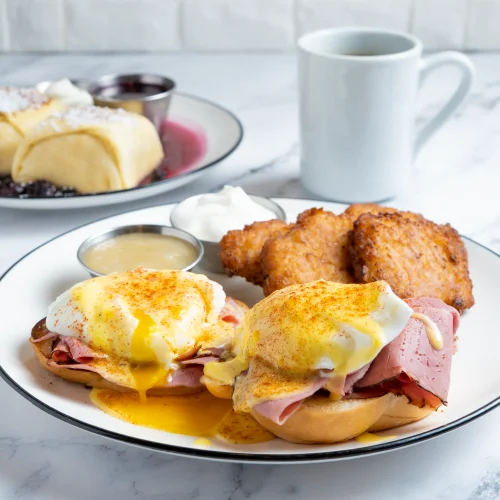 Pastrami eggs Benedict on challah with potato latkes, sour cream, and applesauce