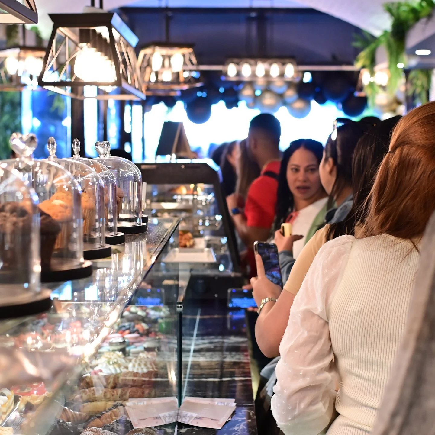 Busy café interior with glass pastry displays and customers in line