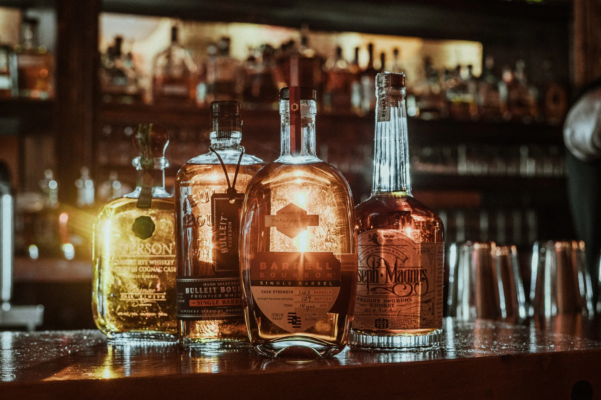 Selection of whiskey bottles on a bar counter with warm lighting.