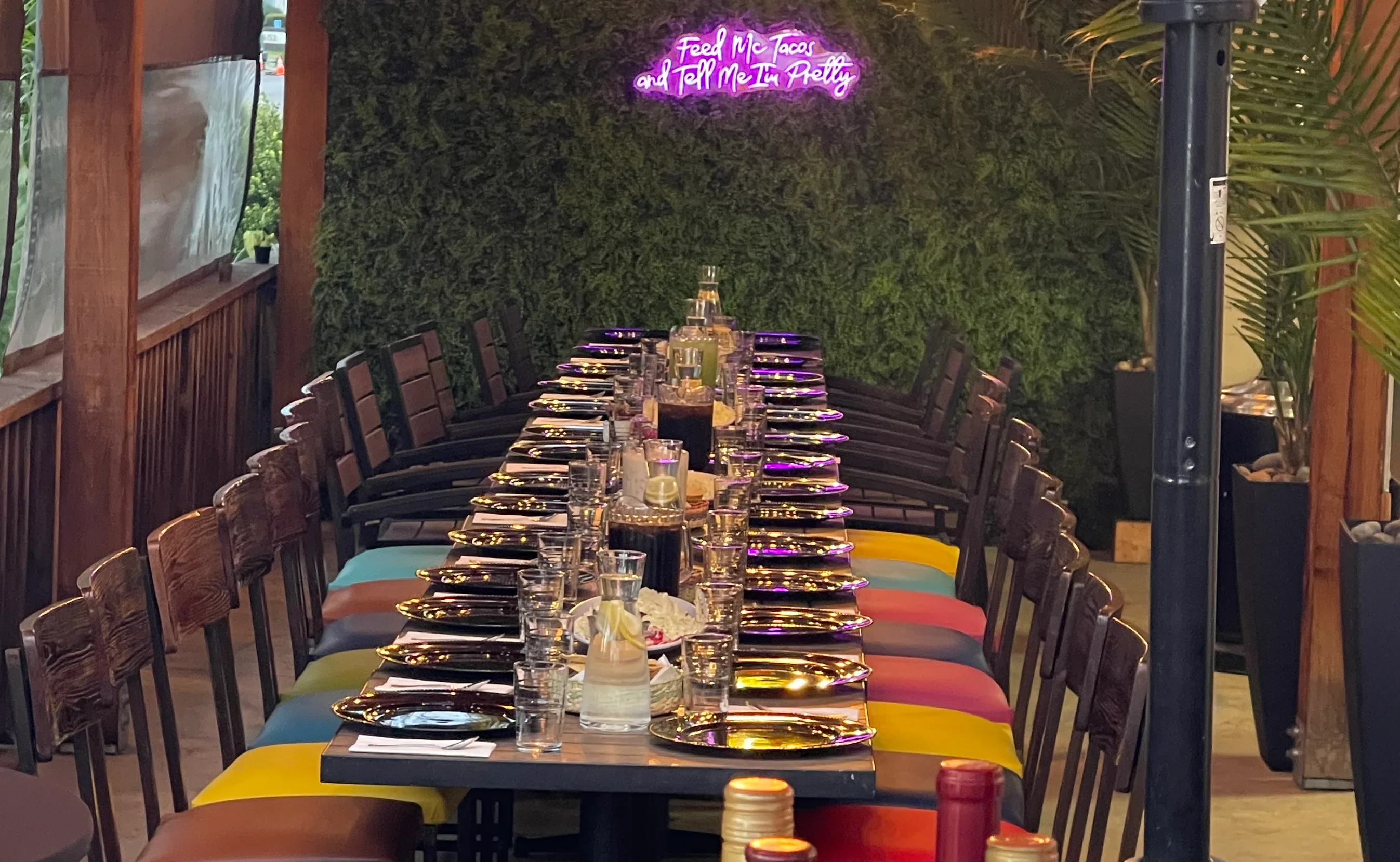 Colorful restaurant dining setup with neon sign and wine bottles