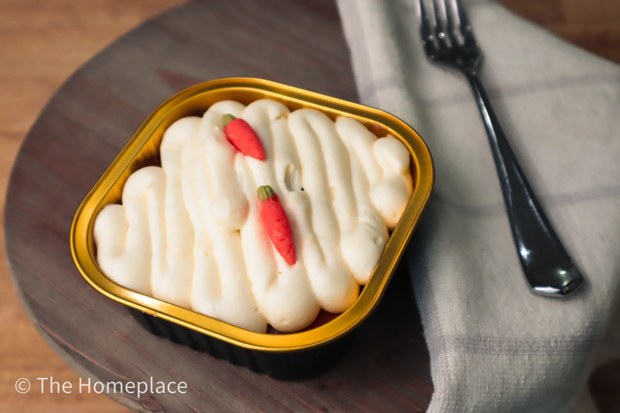 A dessert featuring a creamy frosting topped with small red and green decorative peppers, served in a golden container.
