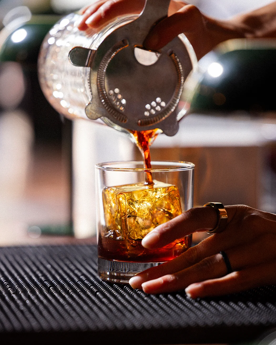 Bartender pouring a cocktail over ice in a glass