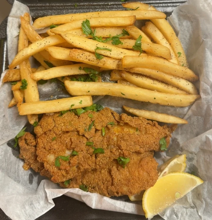 A serving of fried fish accompanied by golden fries, garnished with parsley and served with lemon wedges.