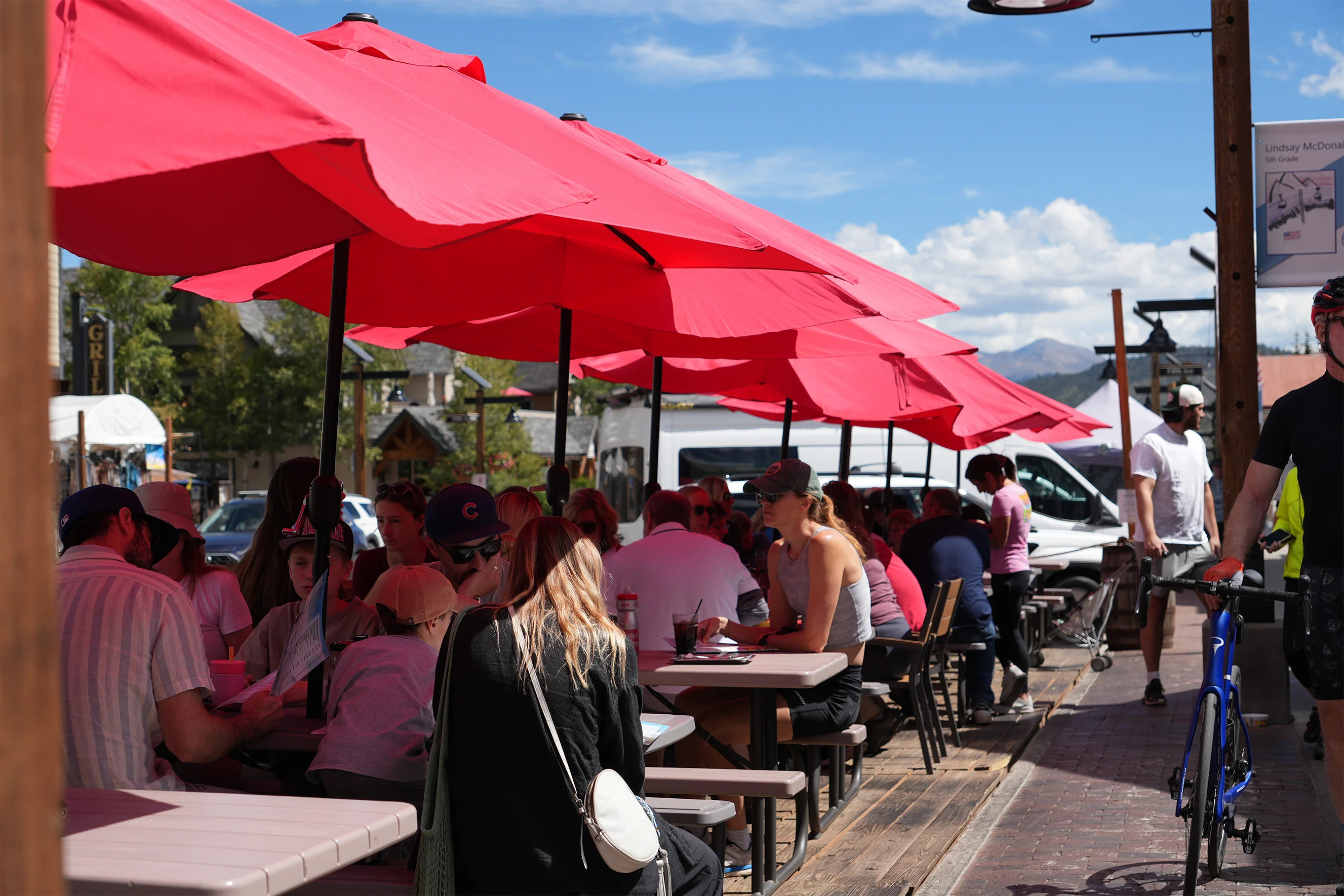 Busy outdoor restaurant patio with red umbrellas and mountain views