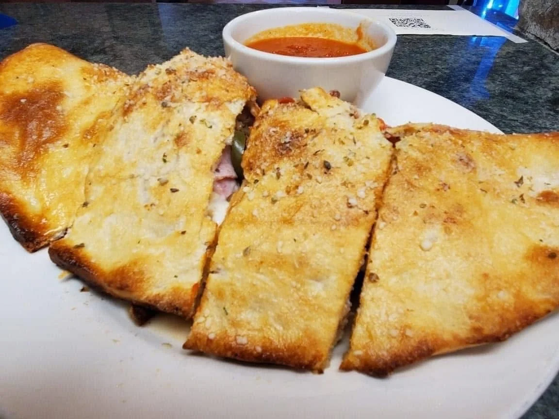 A plate of crispy, golden-browned calzones filled with assorted toppings, served with a side of marinara sauce.