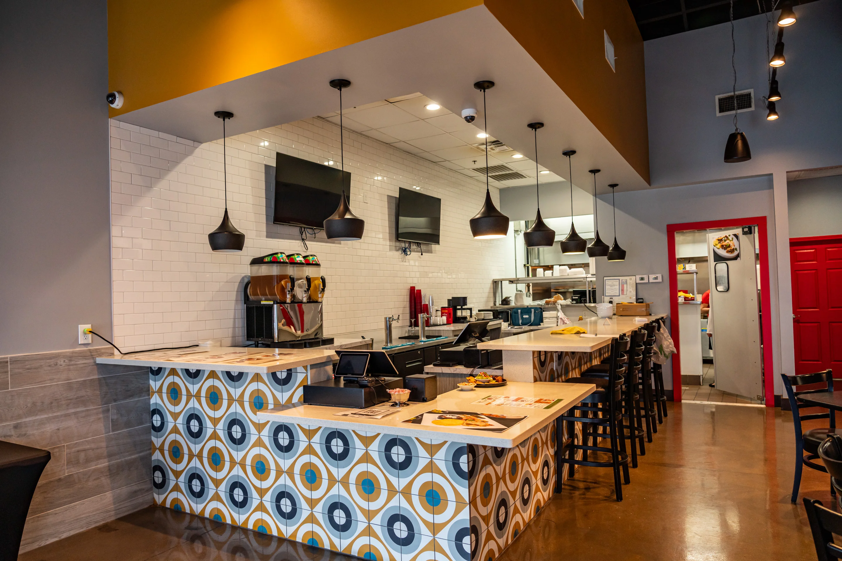 A modern restaurant interior showcasing a bar area with stylish light fixtures and a colorful geometric design.