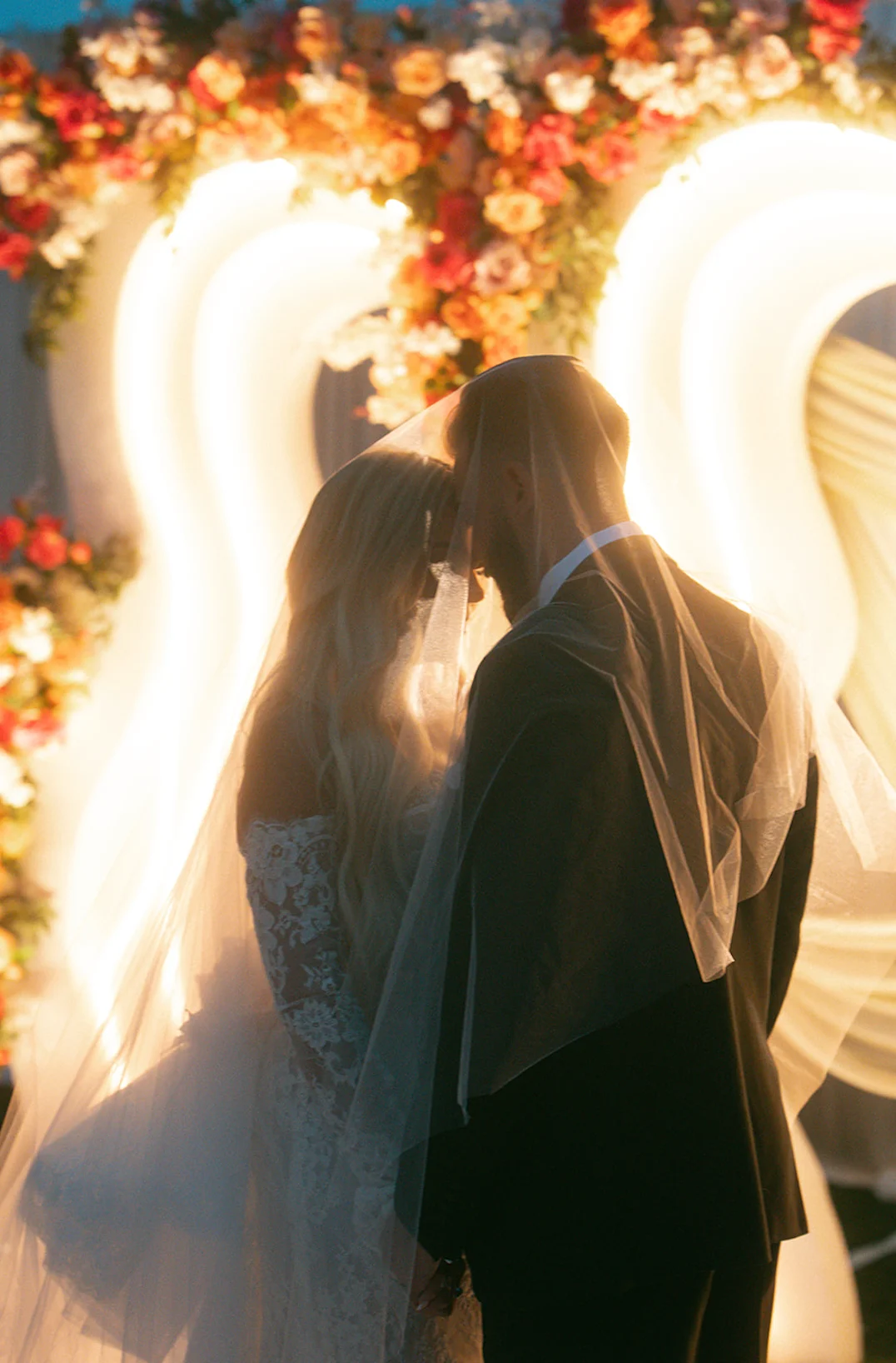 Bride and groom sharing a moment under floral arch at wedding ceremony