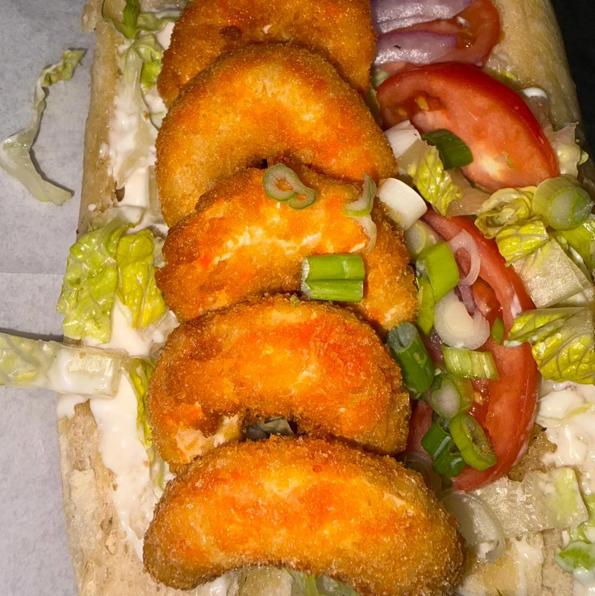 A sandwich filled with crispy fried shrimp, lettuce, tomatoes, and green onions, drizzled with a creamy sauce.
