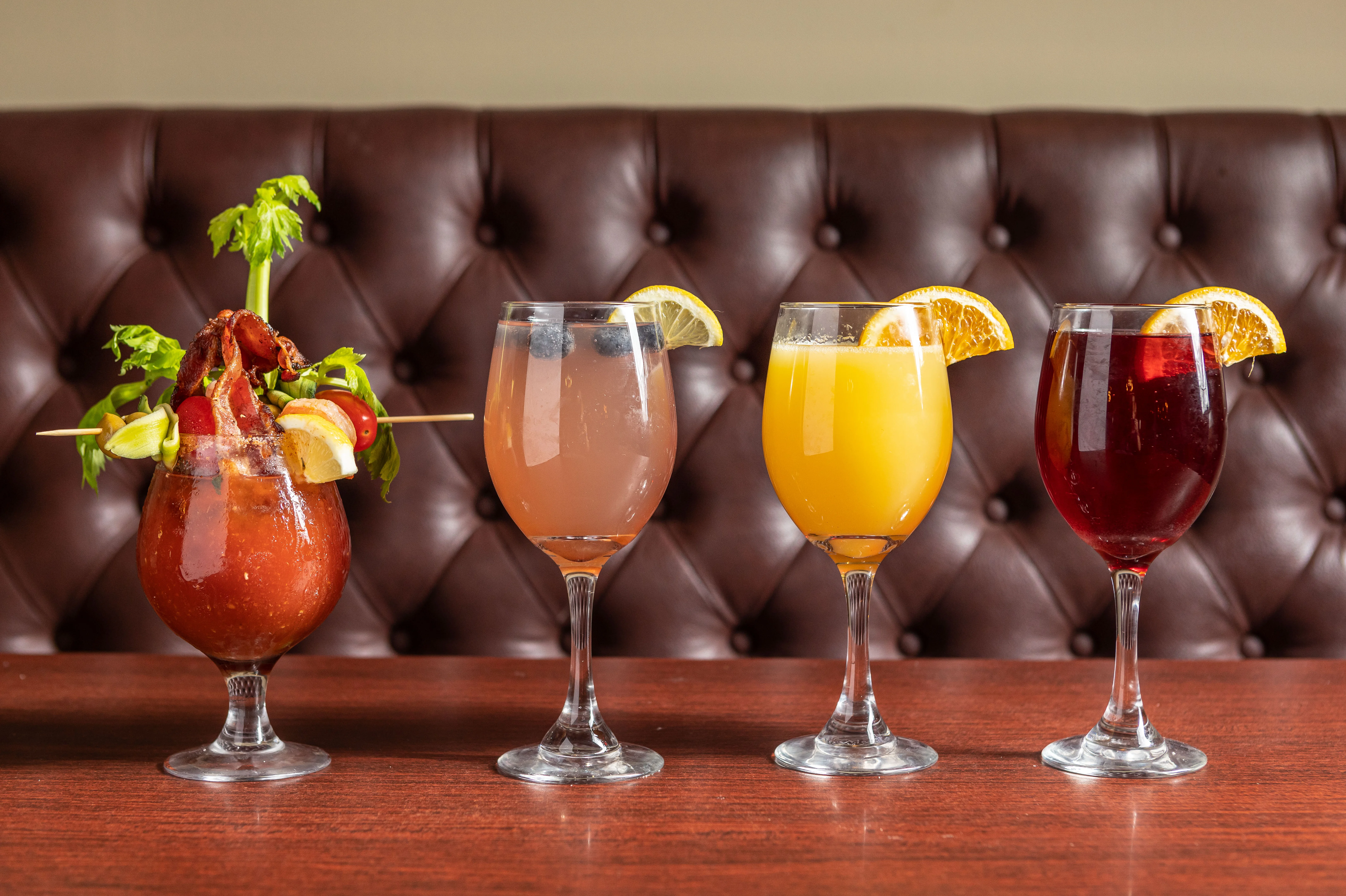 Colorful cocktails including a Bloody Mary and mimosas on a wooden table