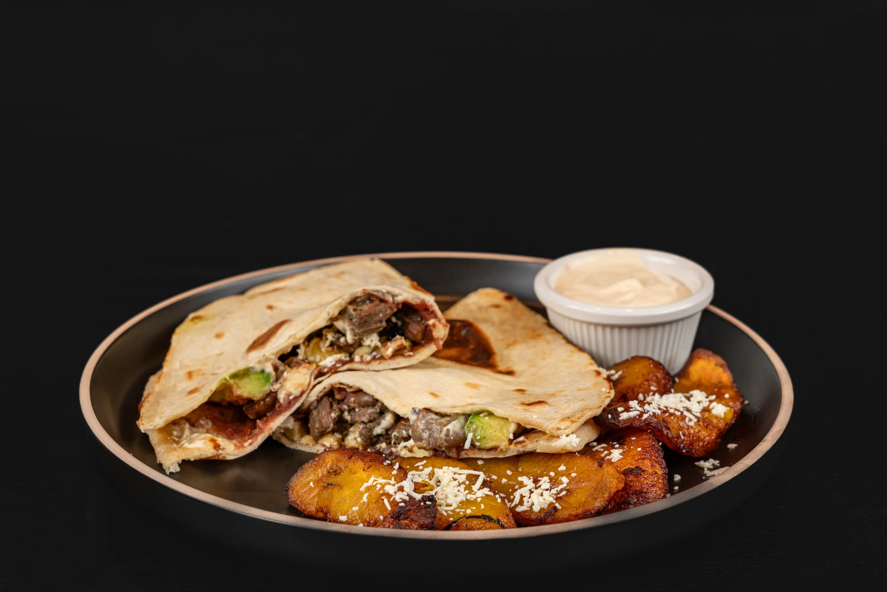 A plate of tortillas filled with beef, accompanied by fried plantains and a small dish of dipping sauce.