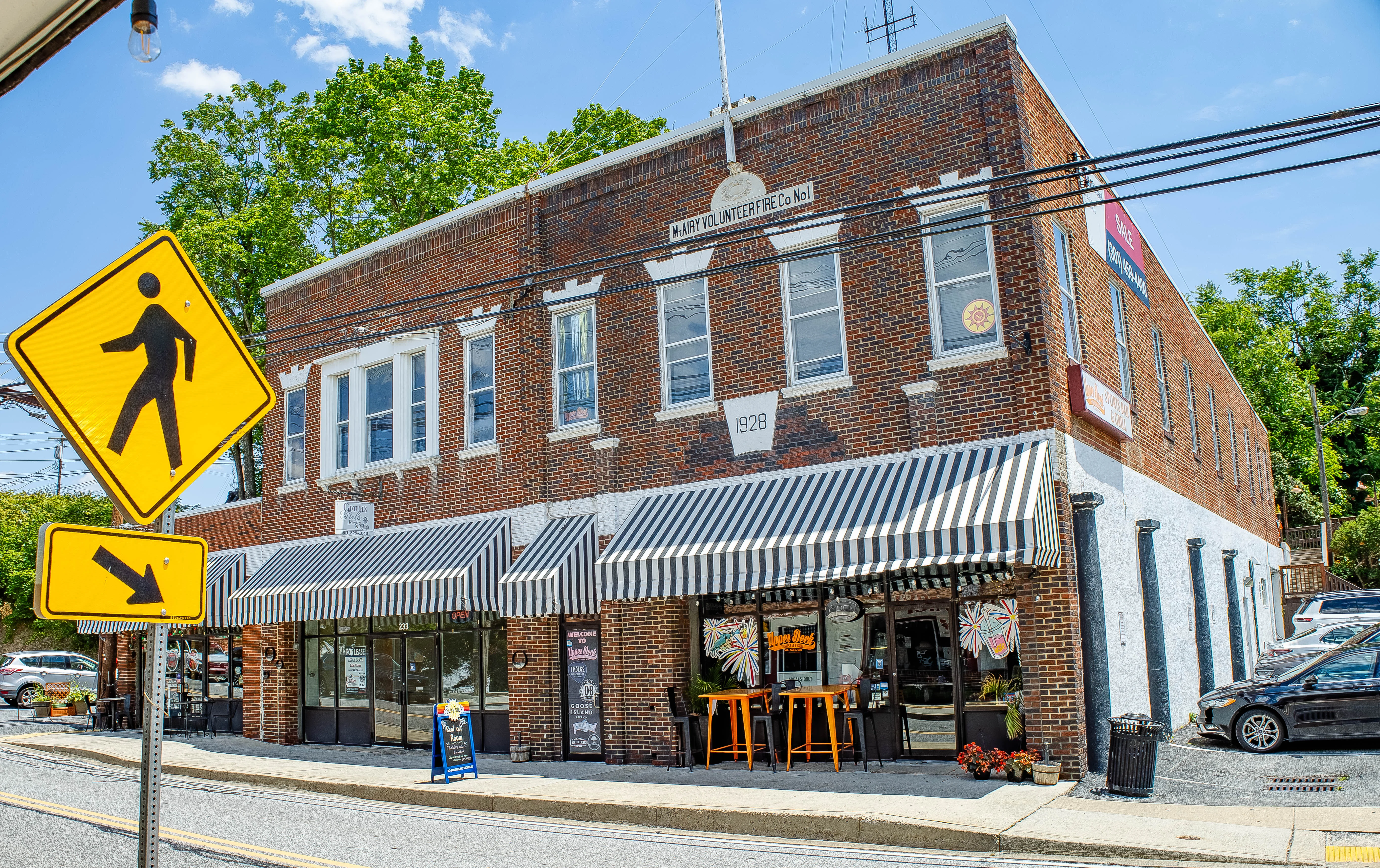 Tilted street view of a brick restaurant storefront with striped awnings and sidewalk signs