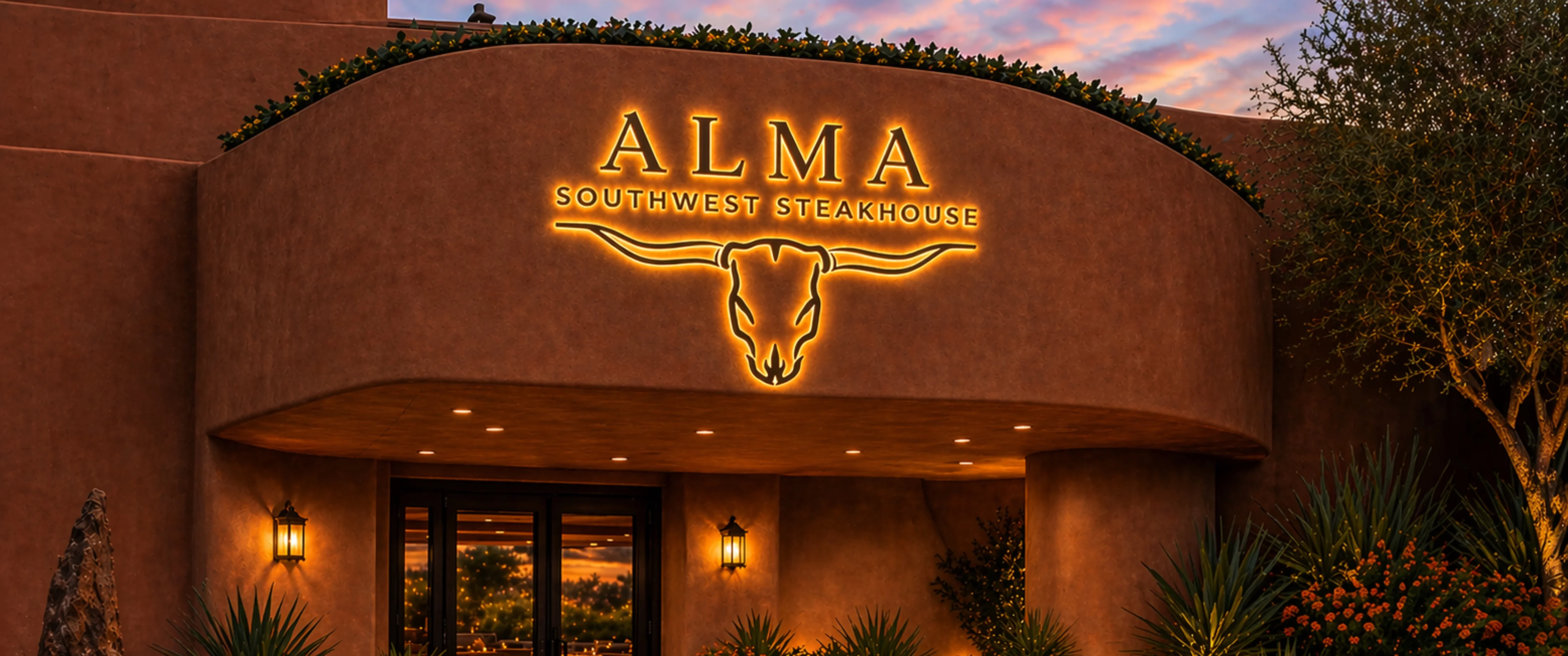 Entrance of Alma Southwest Steakhouse with warm lighting and desert landscaping