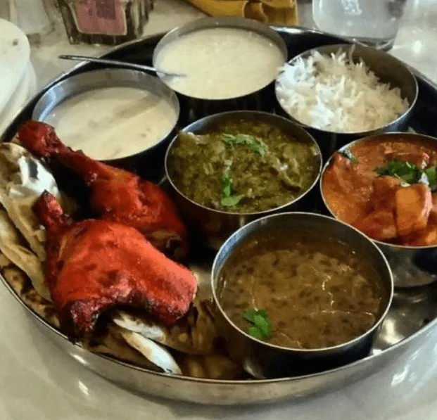 Indian meal with white rice, a two bowl of curry, tandoori chicken ,naan bread, curd and one sweet..