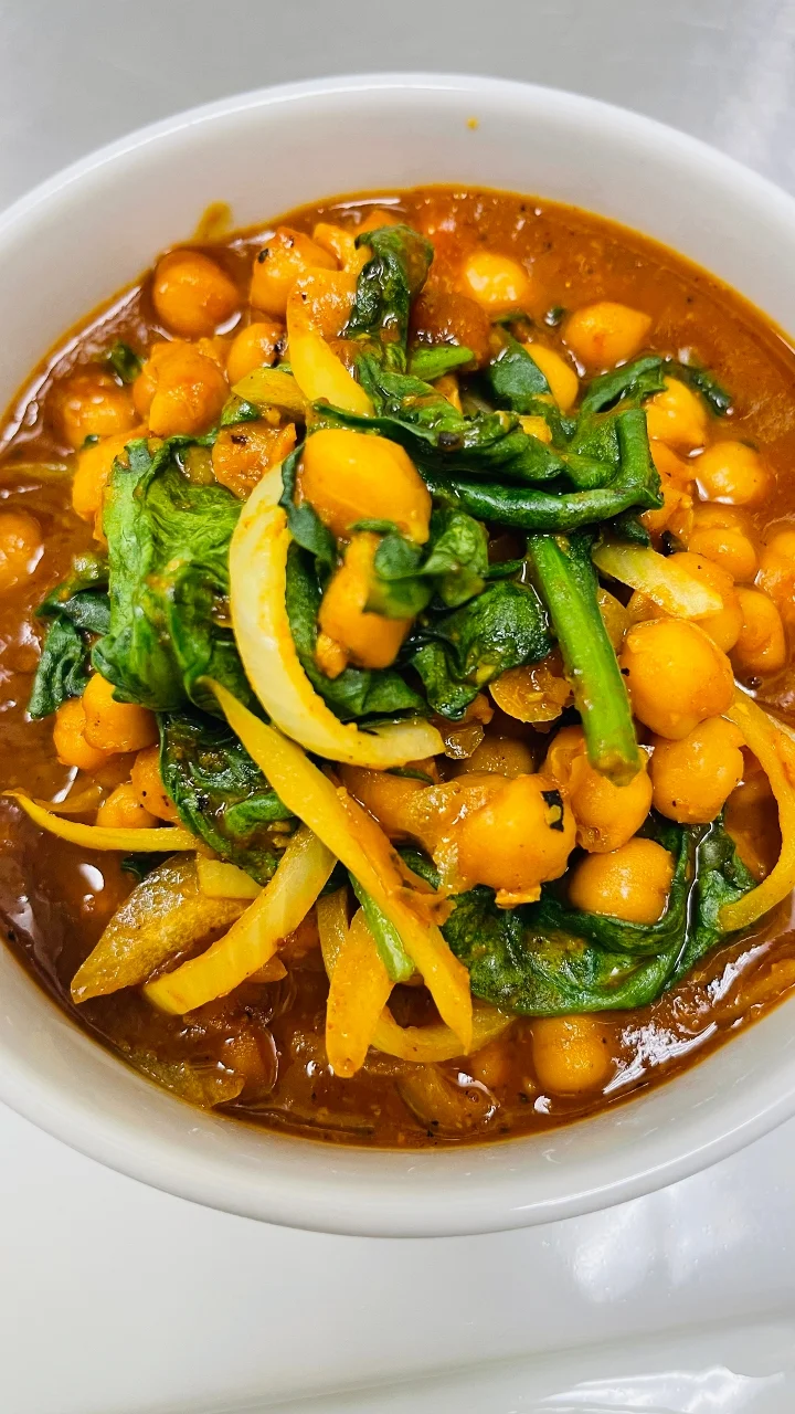 A bowl filled with chickpeas, spinach, onions, and spices, displaying a rich orange sauce that adds flavor and color.